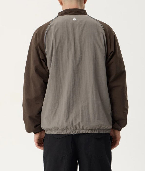 A man wearing a brown and gray color-blocked zip-up jacket with the brand name 'AFENDS' printed in white on the chest, over a white t-shirt and black pants, against a plain light background. SPICY SPORTS SPRAY JACKET OLIVE UNISEX REFLECTIVE PIPING POCKETS