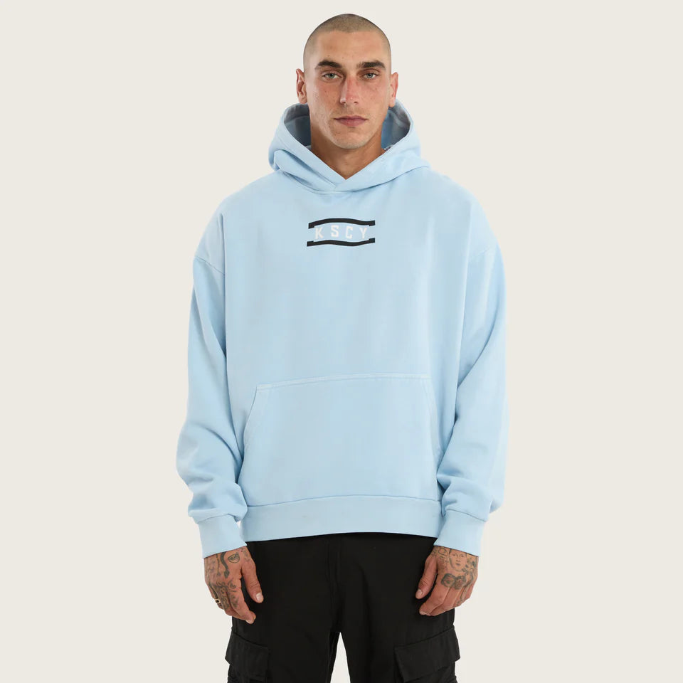 Man wearing a light blue hoodie with a logo on a beige background