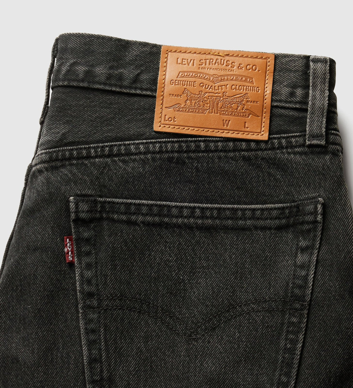Close-up of the back waistband of Levi's 501 jeans in washed black denim, showing the signature brown leather patch with the brand name and a small red tab on the pocket.