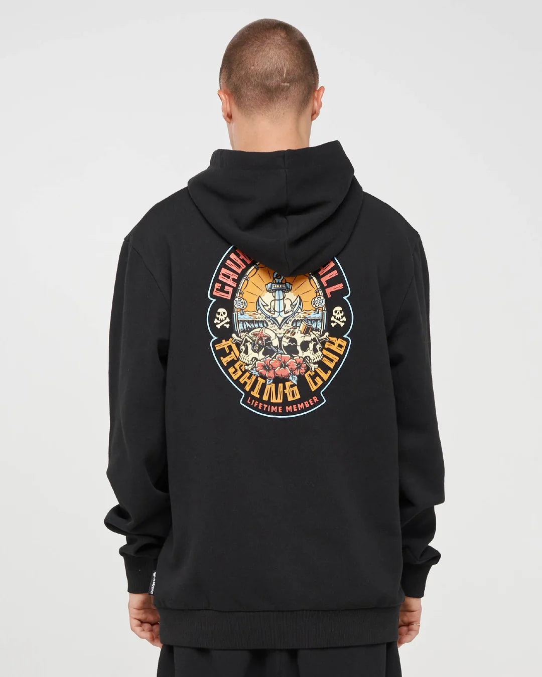 A man viewed from behind wearing a black pullover hoodie with a large circular graphic print on the back. The graphic features a skull, ship, and the words 'CHILE BULL ESCUDAR CLUB' in orange, yellow, and white.