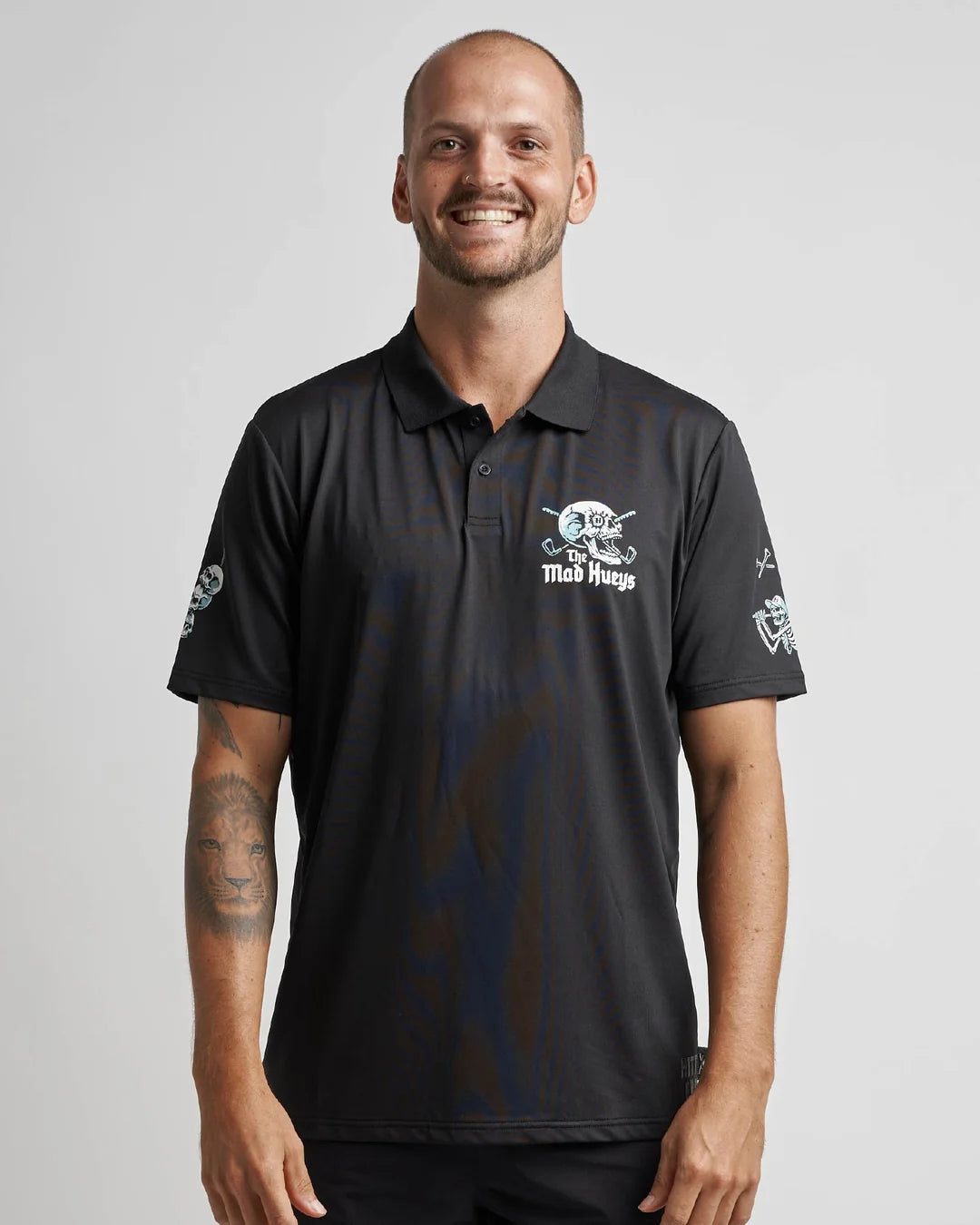 A smiling man wearing a black short-sleeve polo shirt with white graphics on the chest and sleeves, photographed against a light gray studio background.