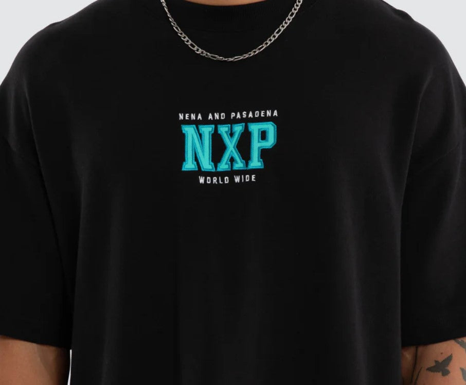 A person shown from the back wearing a black oversized T-shirt with a large turquoise and white graphic reading 'NENA AND PASADENA Upscale Supply WORLD WIDE MISSION' on a light gray studio background. WEST LOOPBACK RAPTOR TEE ANTHRACITE