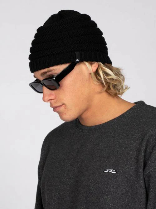 Person wearing a black beanie and sunglasses with a gray sweatshirt featuring a logo.