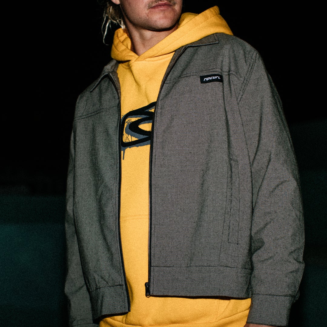 Person wearing a gray jacket over a yellow hoodie with a visible brand logo.