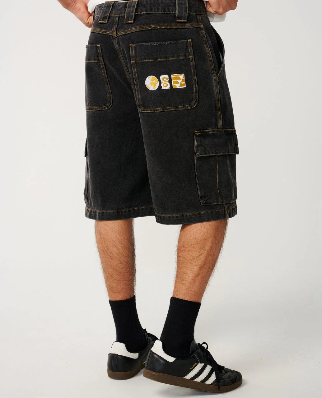 Black cargo shorts with a logo on the pocket worn by a person on a white background