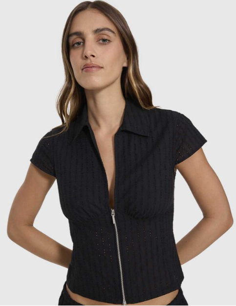 A woman modeling a black ribbed short-sleeve crop top with a front zipper, paired with a matching black textured skirt, against a plain white background. DANICA BRODERIE ANGLAISE TOP THRILLS BLACK LADIES TOP COLLAR ZIP