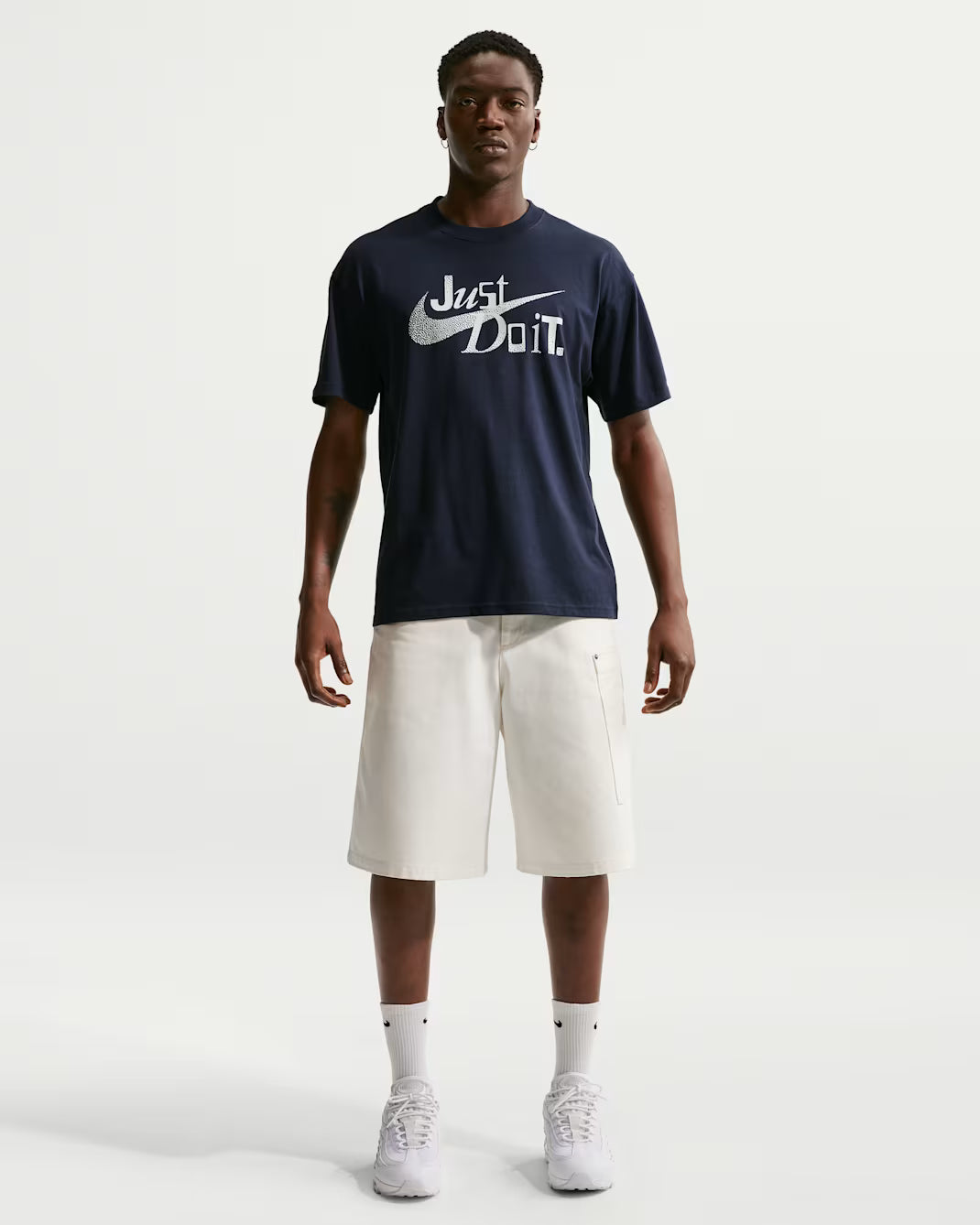 Person wearing a navy blue t-shirt with a logo and white shorts on a white background