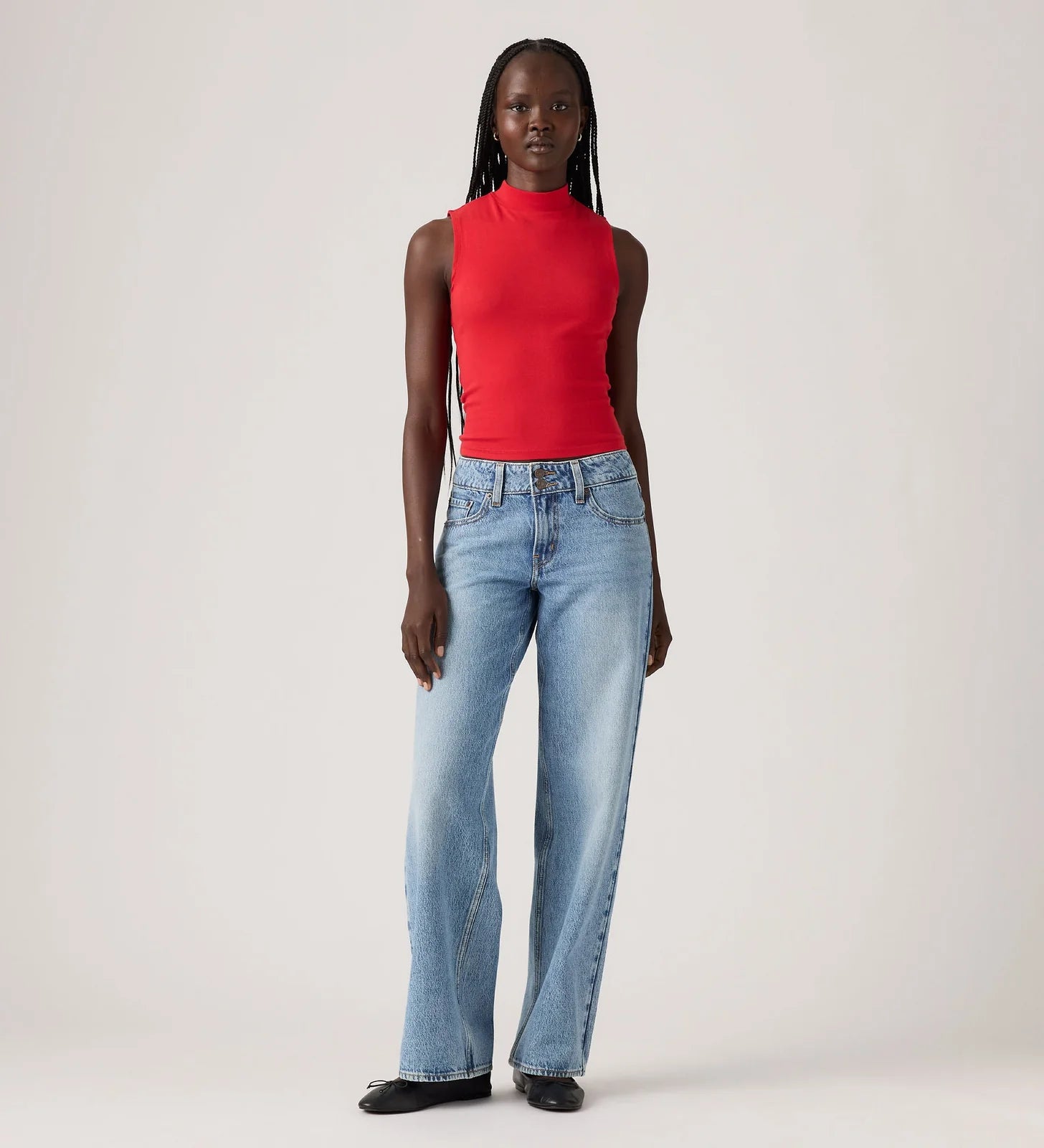 Person wearing a red sleeveless top and light blue jeans on a white background