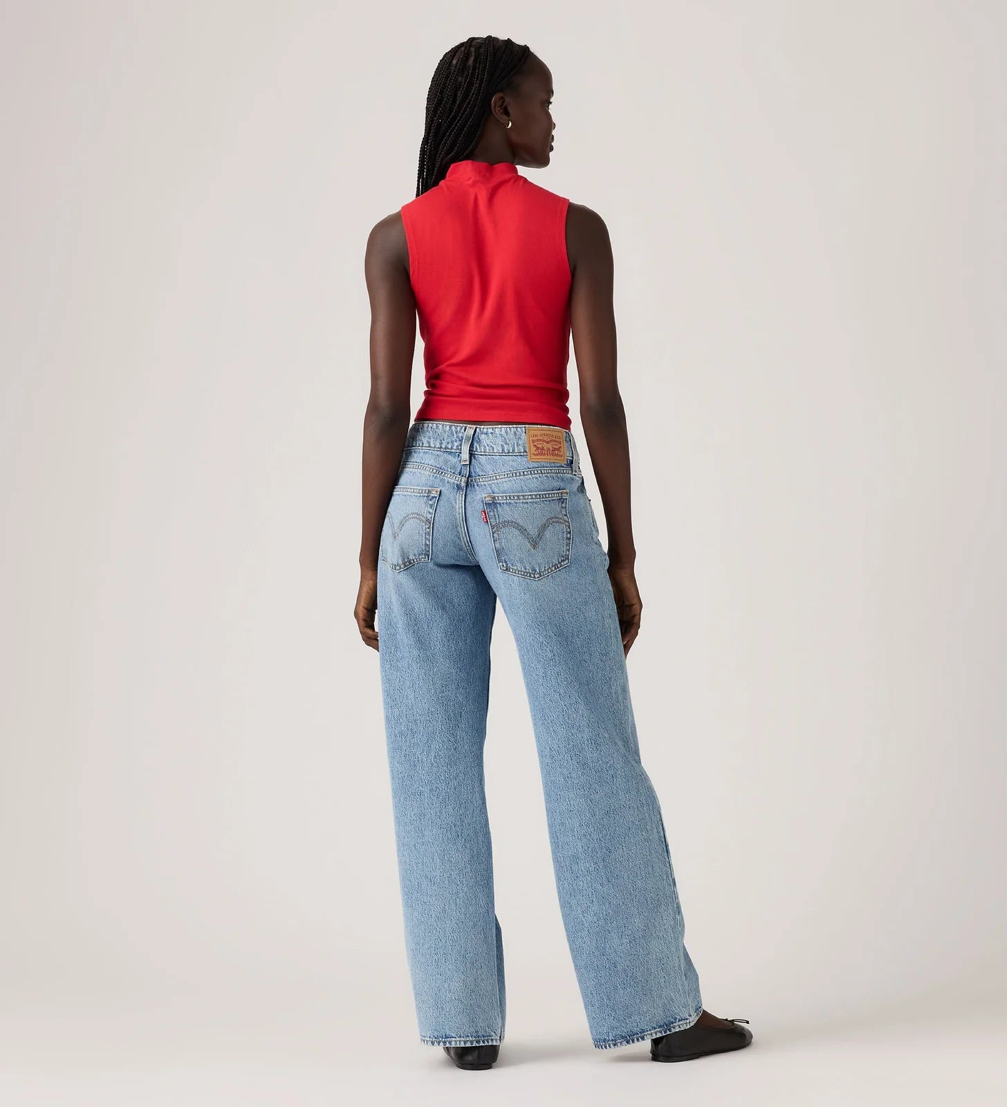 Person wearing a red sleeveless top and light blue jeans on a plain background