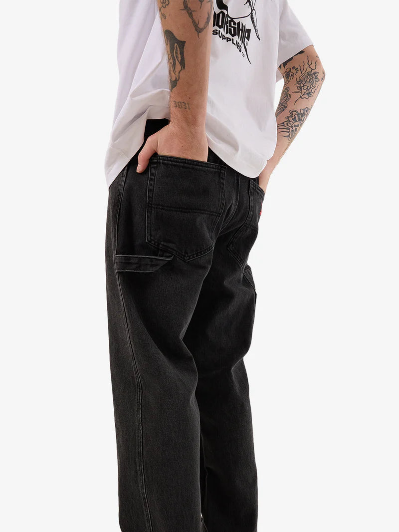 Person wearing black pants and a white shirt with tattoos on arms, standing against a white background