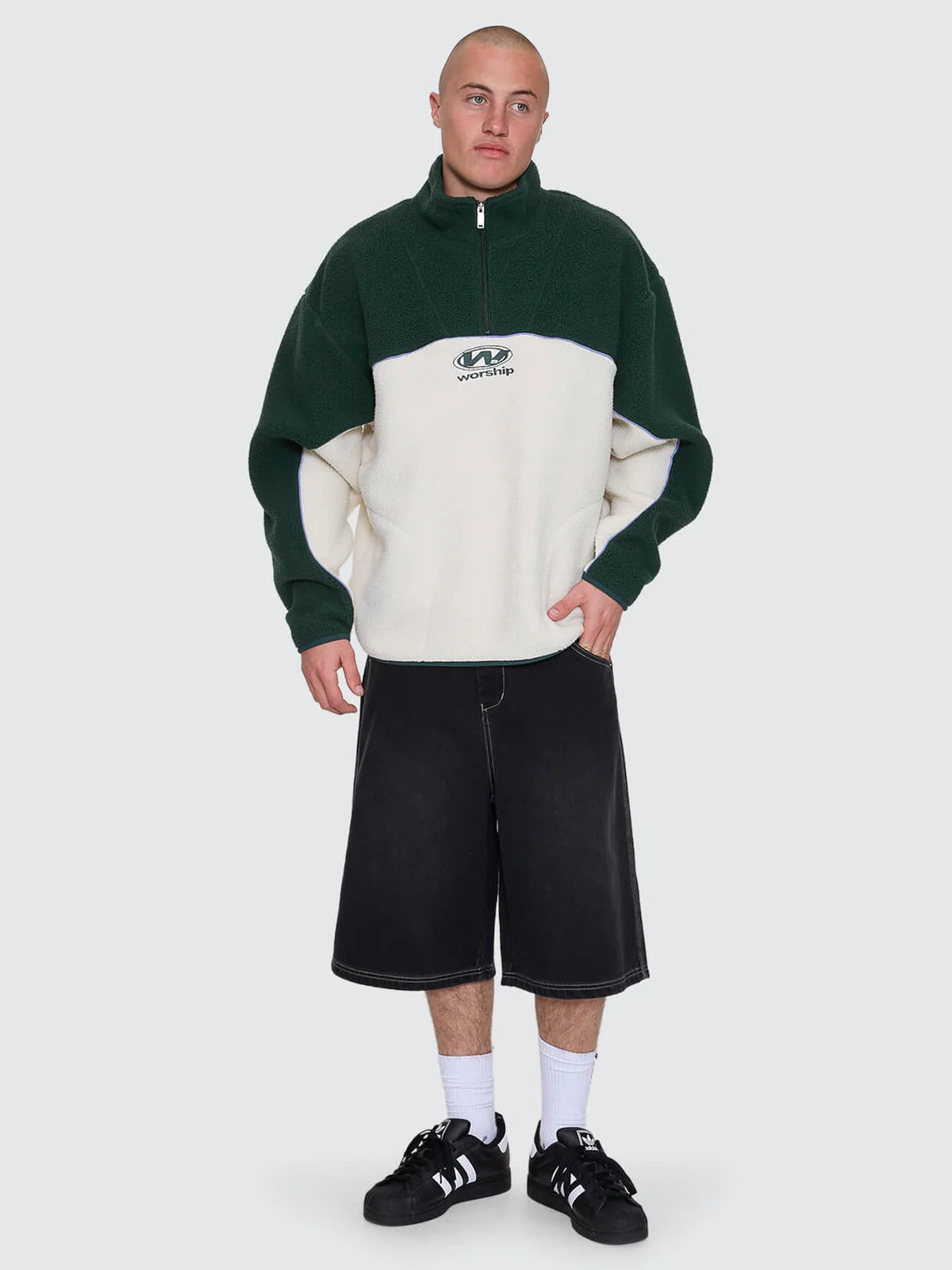 Person wearing a green and beige sweater with black shorts on a white background