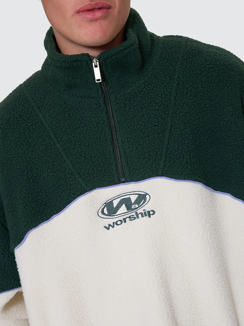 Close-up of a green and white fleece pullover with 'worship' logo on a gray background
