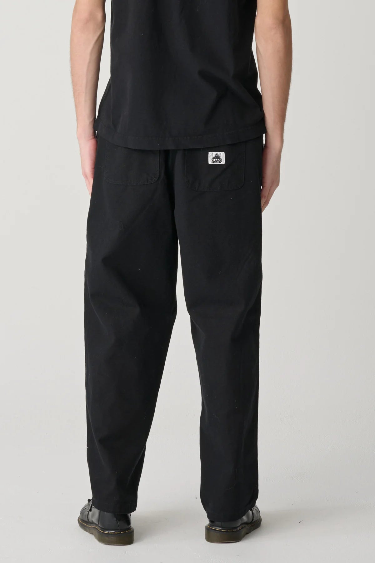 Person wearing black pants with an XLarge logo on a white background