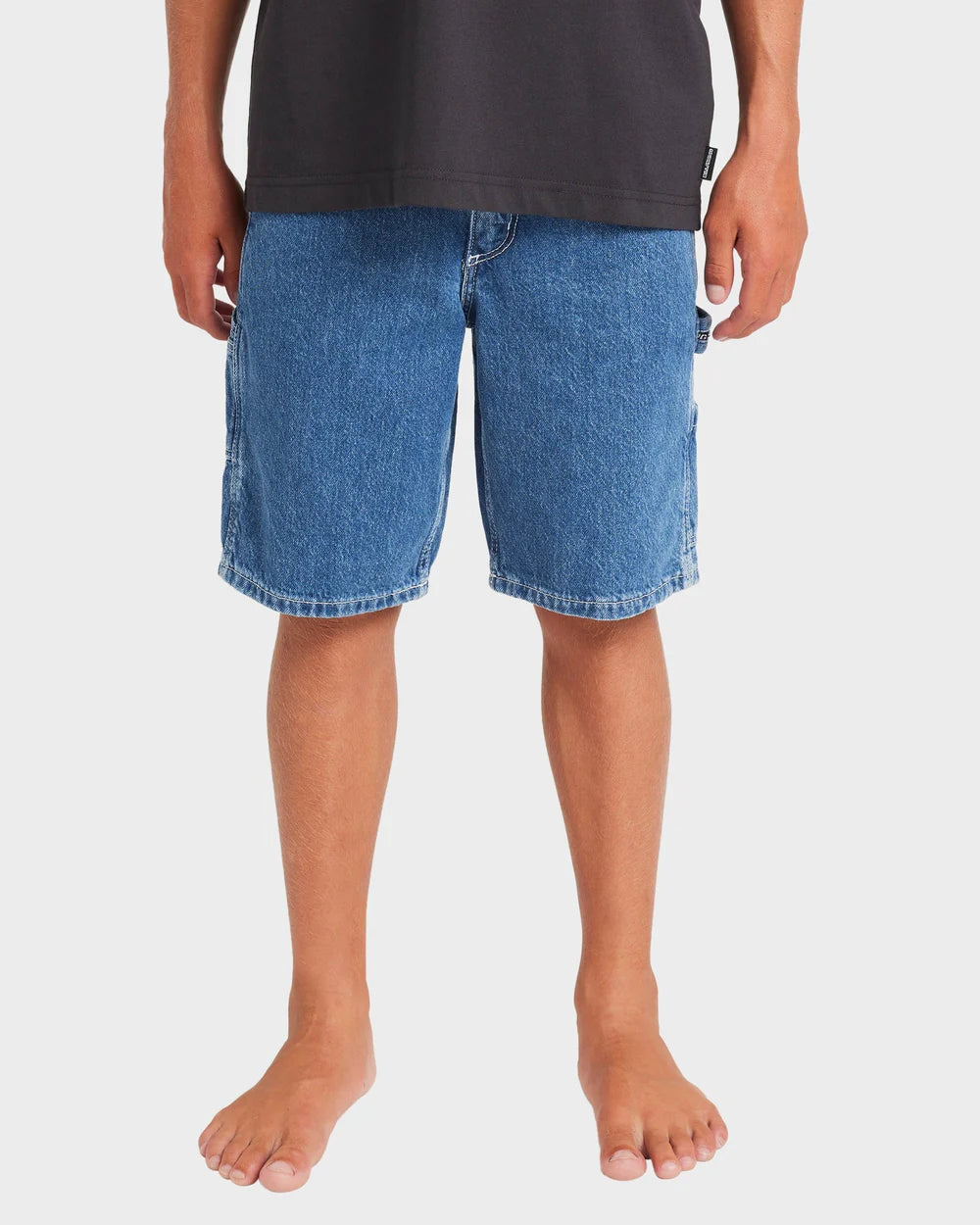 Person wearing blue denim shorts and a black shirt on a white background