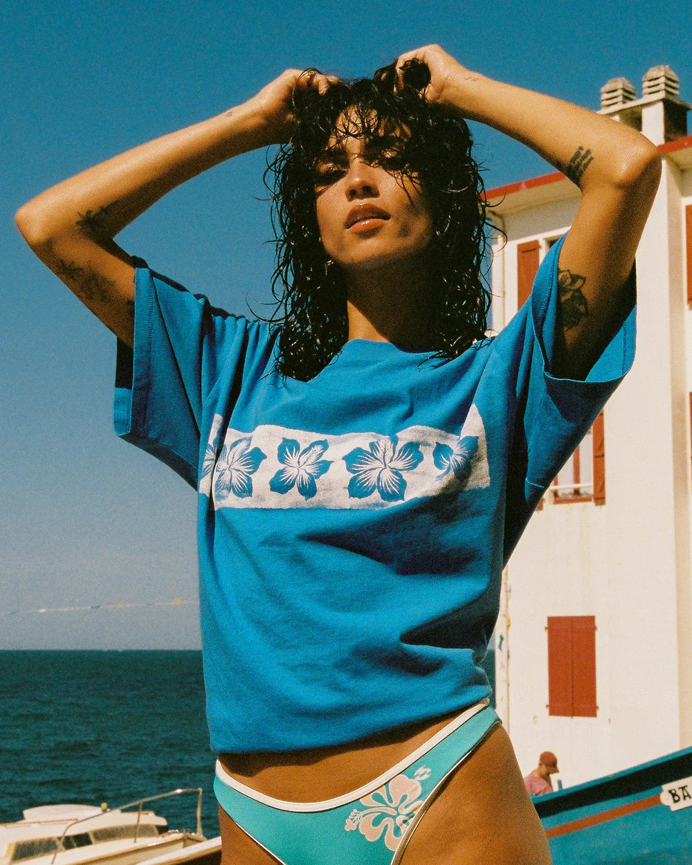 Woman wearing a blue floral-patterned shirt and green bikini bottom by the sea.