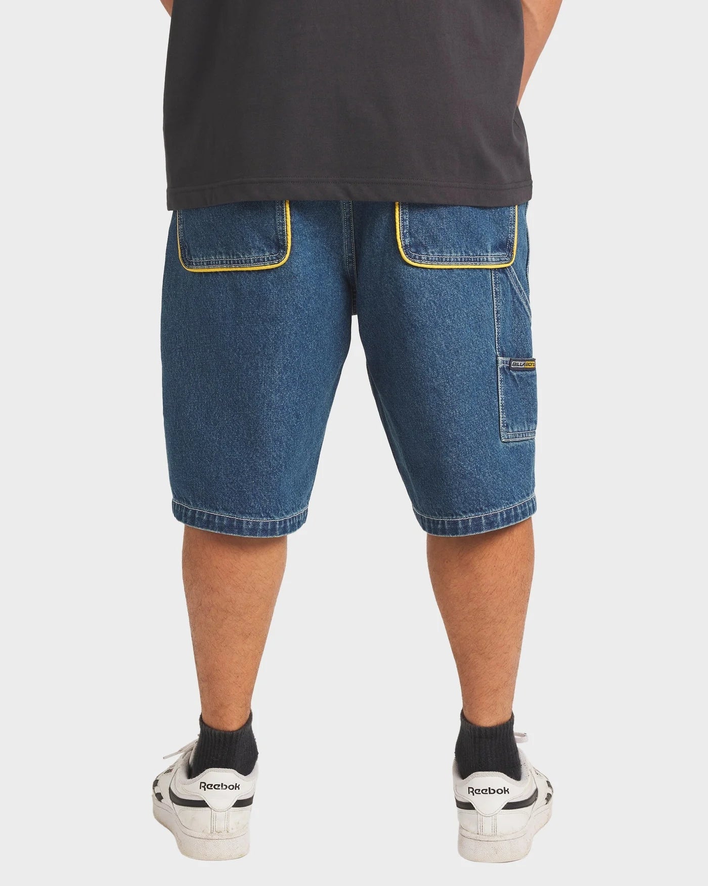 Person wearing blue denim shorts with yellow stitching on a white background
