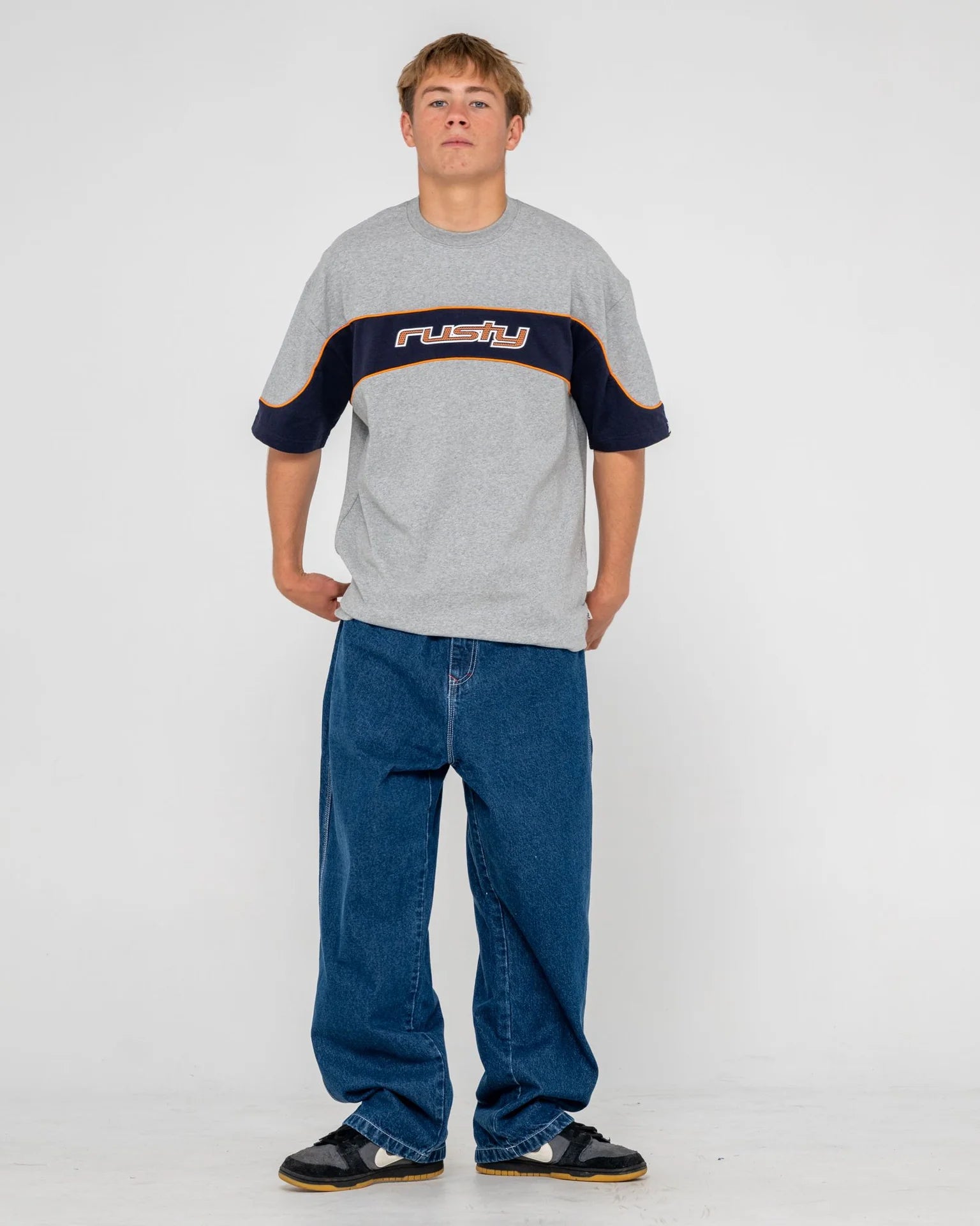 Person wearing a gray t-shirt with a logo and blue jeans on a white background