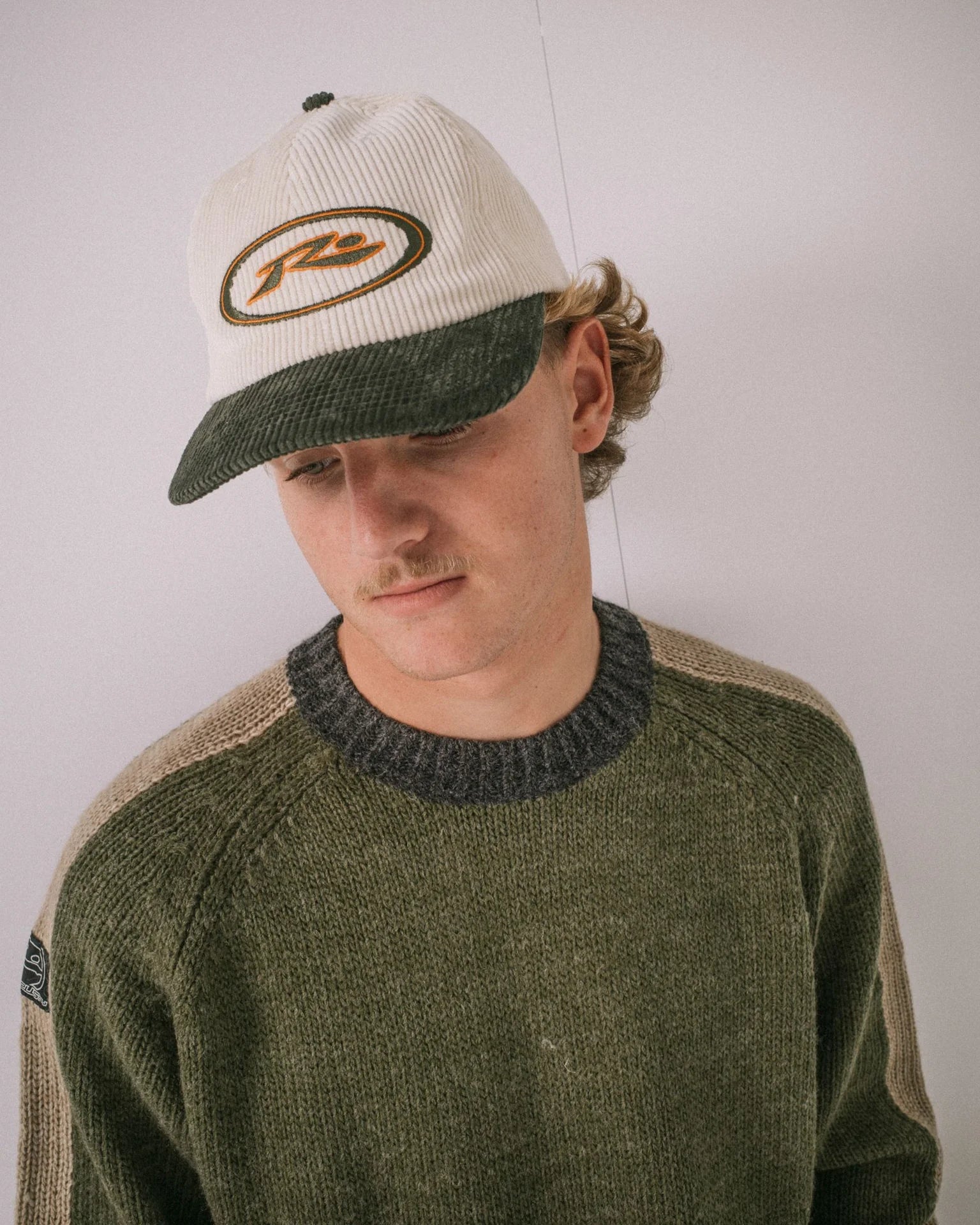 Person wearing a cap and sweater with a neutral background