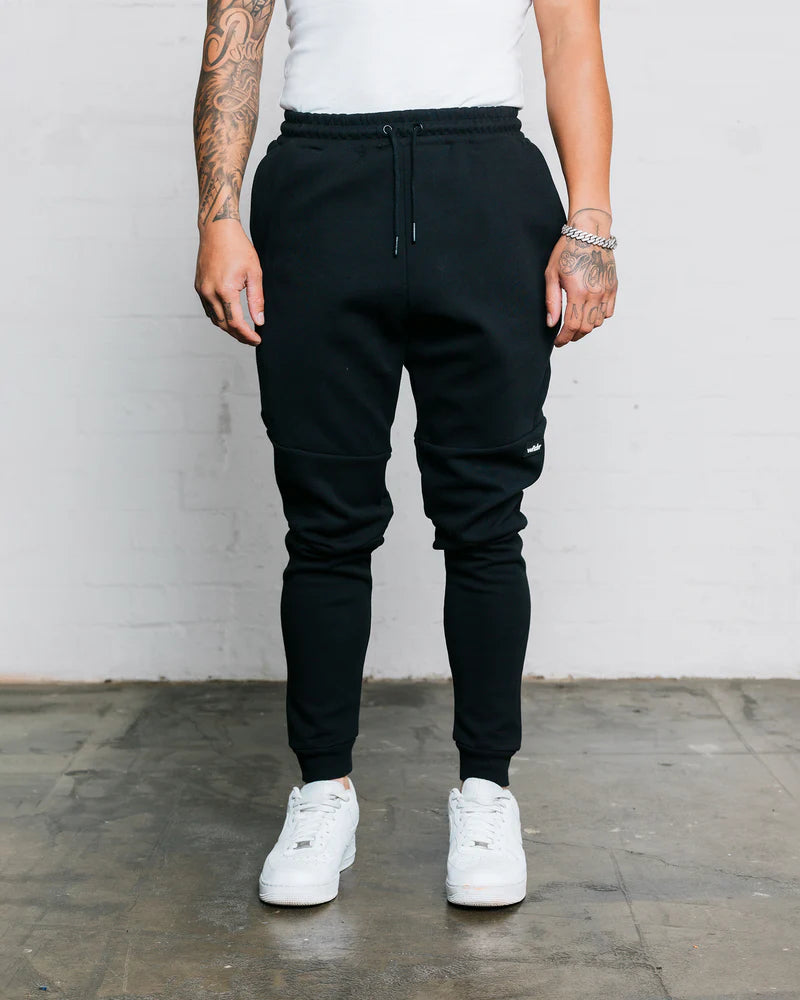 Person wearing wndrr black jogger pants and white sneakers against a plain background