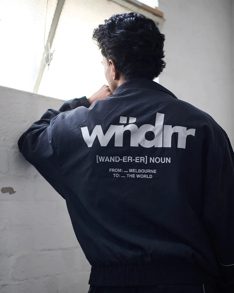 Person wearing a black jacket with 'wndrr' branding, standing against a light-colored wall.