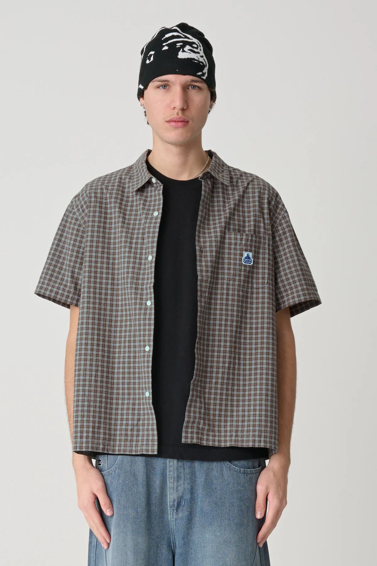 Person wearing a Xlarge checkered shirt, black beanie, and jeans on a plain background