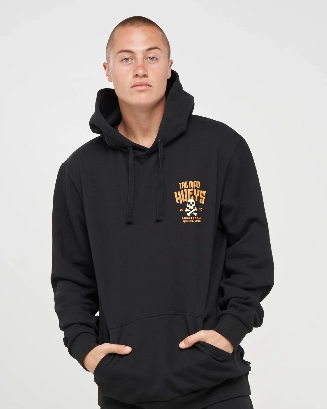 A man wearing a black pullover hoodie with a yellow and white graphic on the left chest that reads 'THE GED HUFFS' with a skull and crossbones, photographed against a light gray studio background.