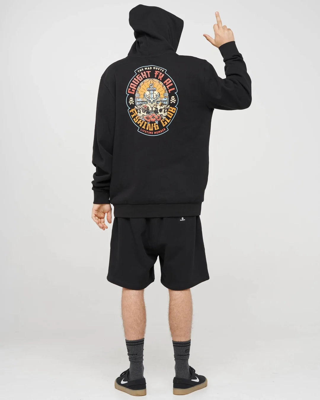A model shown from the back wearing a black hoodie with a large multicolor graphic on the back, black shorts, and black sneakers, against a light gray studio background.