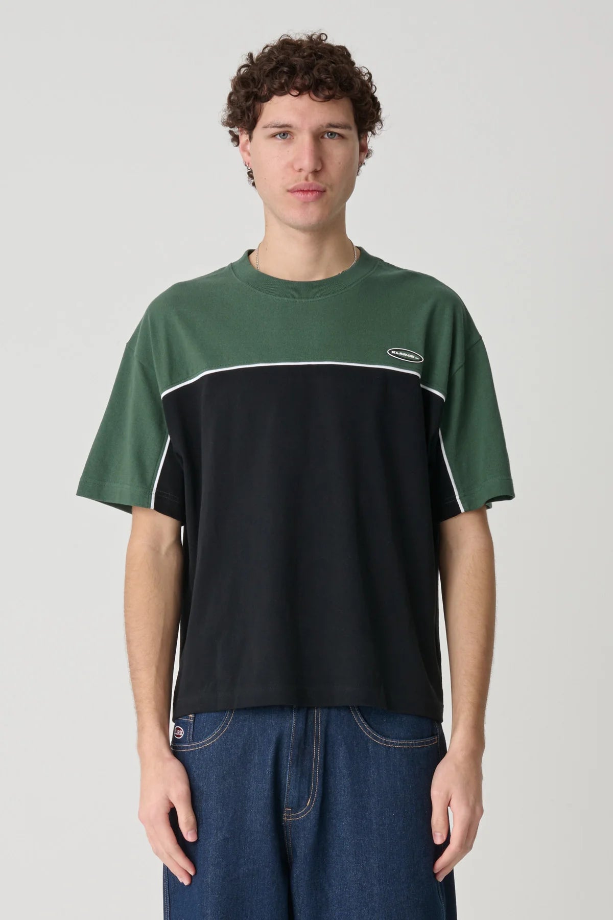 Person wearing a green and black t-shirt with a logo on a plain background