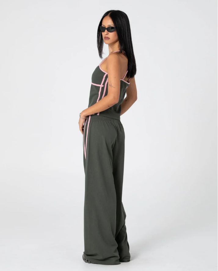A person shown from the back wearing loose, wide-leg sweatpants in an olive green color, paired with a matching dark top, against a plain white studio background. SISTER BRONSON LOW RISE WIDE LEG PANT SPB GREEN PINK WIDE LEG TRACKPANT LADIES RUSTY
