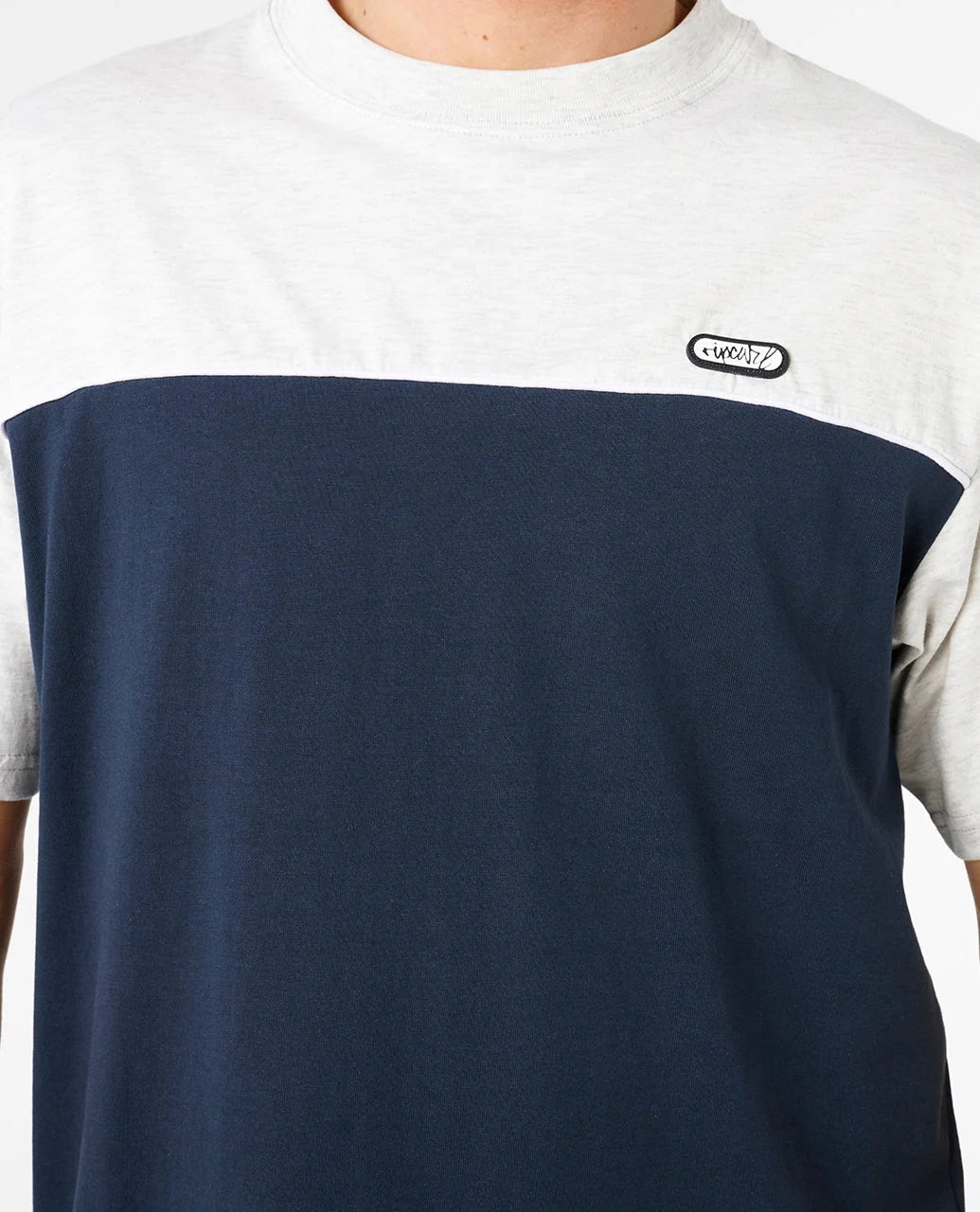 Person wearing a two-tone t-shirt with a navy blue front and light gray sleeves and collar, featuring a logo on the chest.