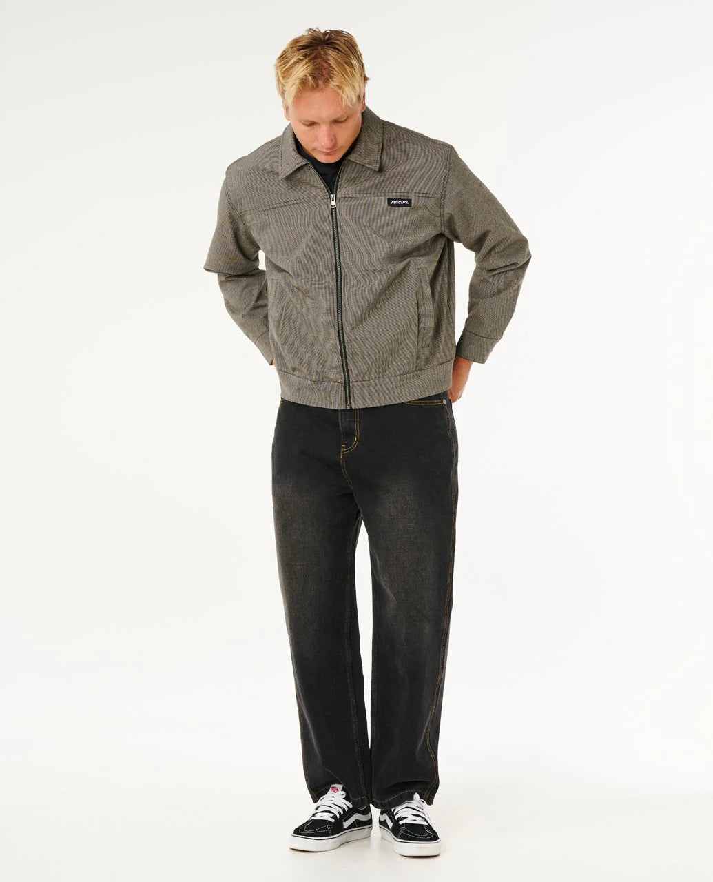 Man wearing a patterned jacket and dark jeans on a white background