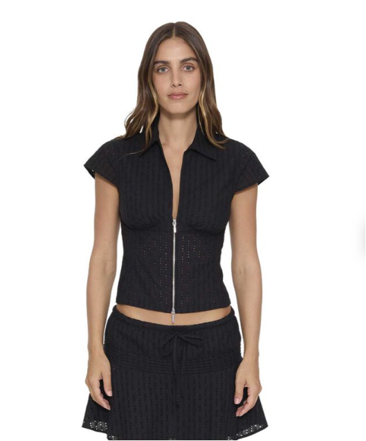 A woman modeling a black ribbed short-sleeve crop top with a front zipper, paired with a matching black textured skirt, against a plain white background. DANICA BRODERIE ANGLAISE TOP THRILLS BLACK LADIES TOP COLLAR ZIP
