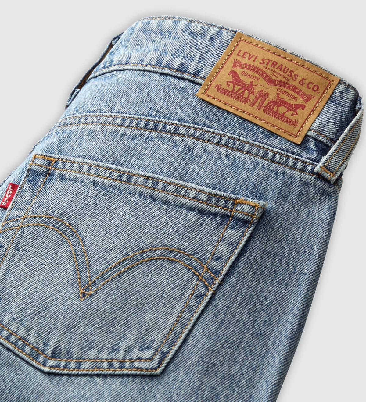 Close-up of the back pocket of light-wash blue Levi's jeans, showing the iconic curved stitching, a portion of the red tab, and the brown leather Levi's patch on the waistband.
