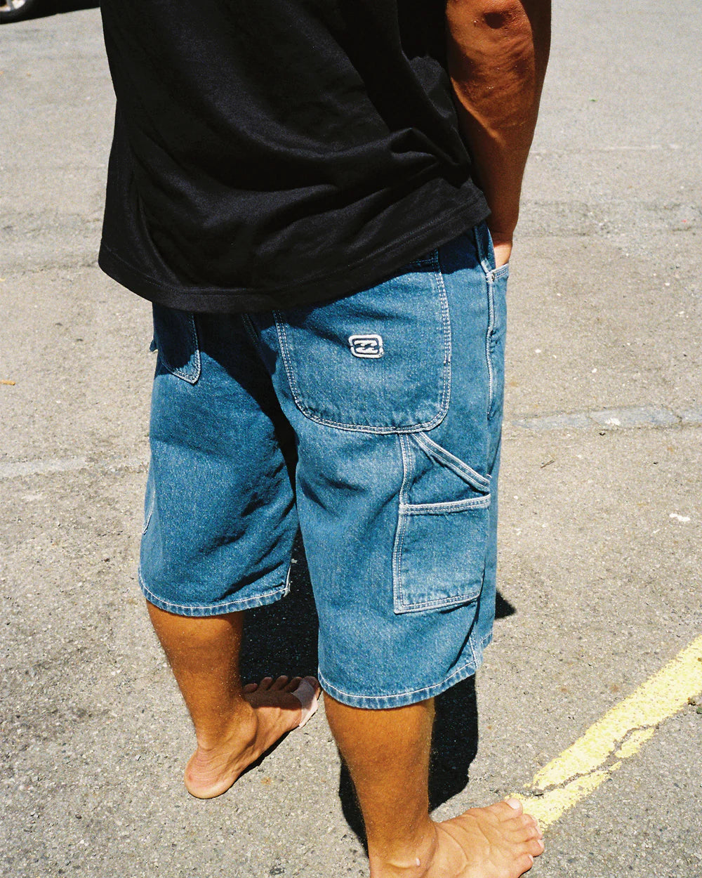 Person wearing blue denim shorts with a brand logo on a street.