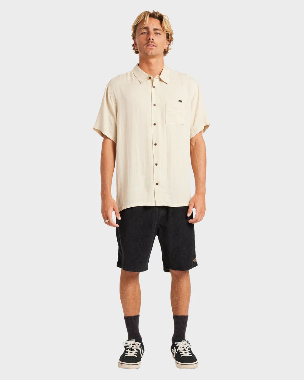Man wearing a beige short-sleeve shirt and black shorts on a white background