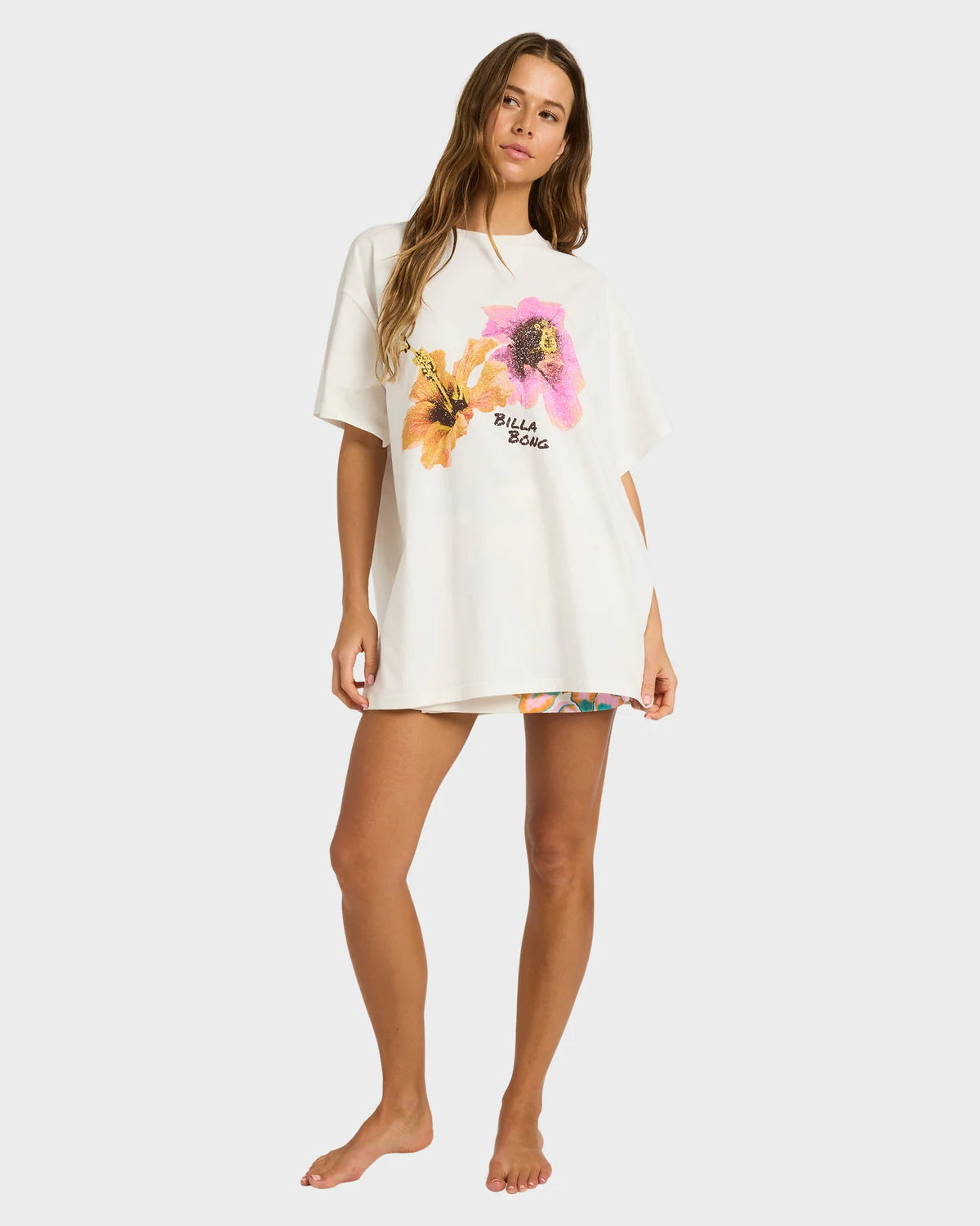 Woman wearing a white oversized t-shirt with floral designs and text on a plain background