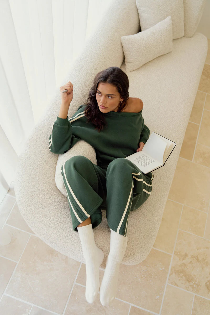 Woman in green tracksuit sitting on a white chair holding a book.