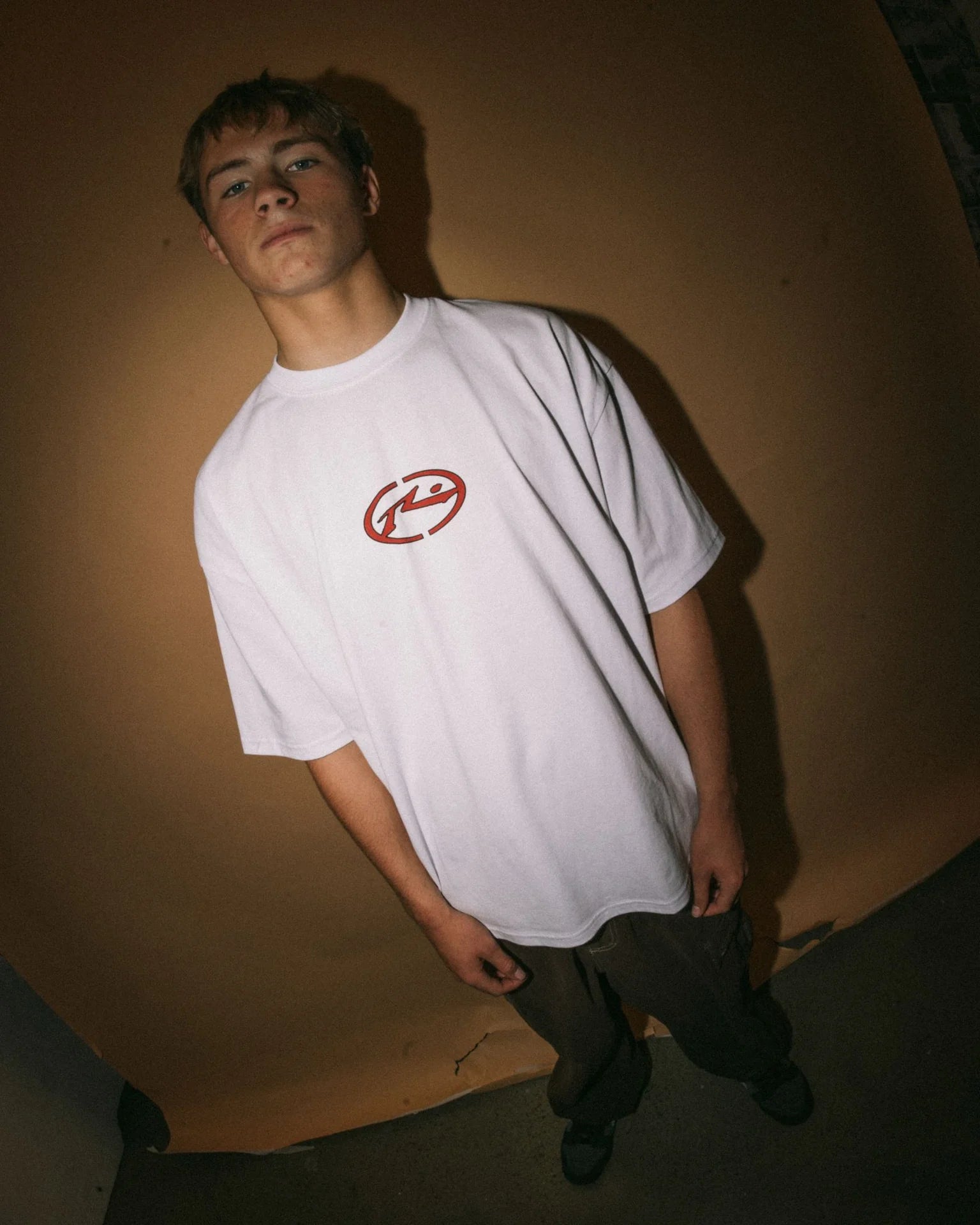 Person wearing a white t-shirt with a red logo against a plain background