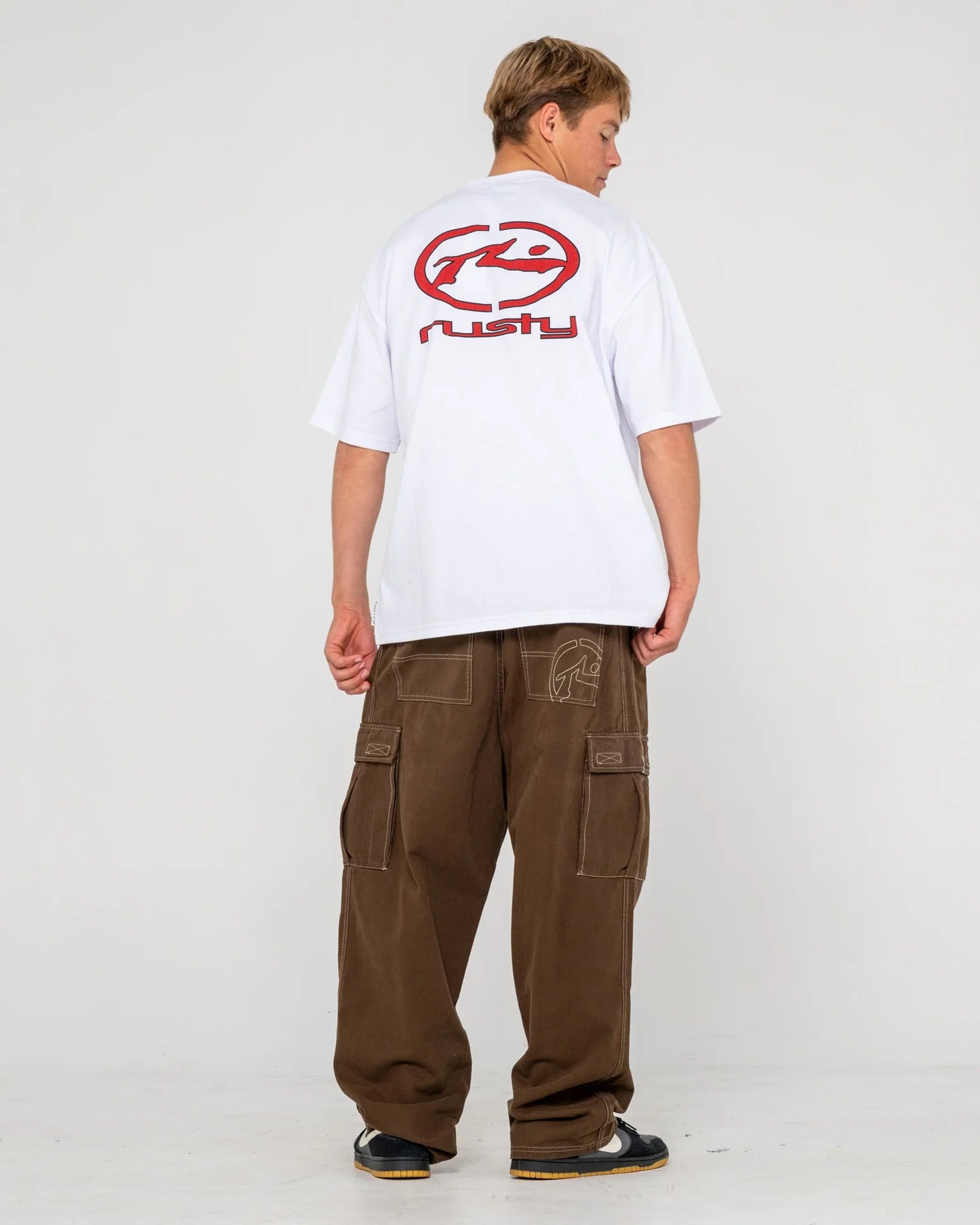 Person wearing a white t-shirt with a red logo and brown cargo pants on a white background