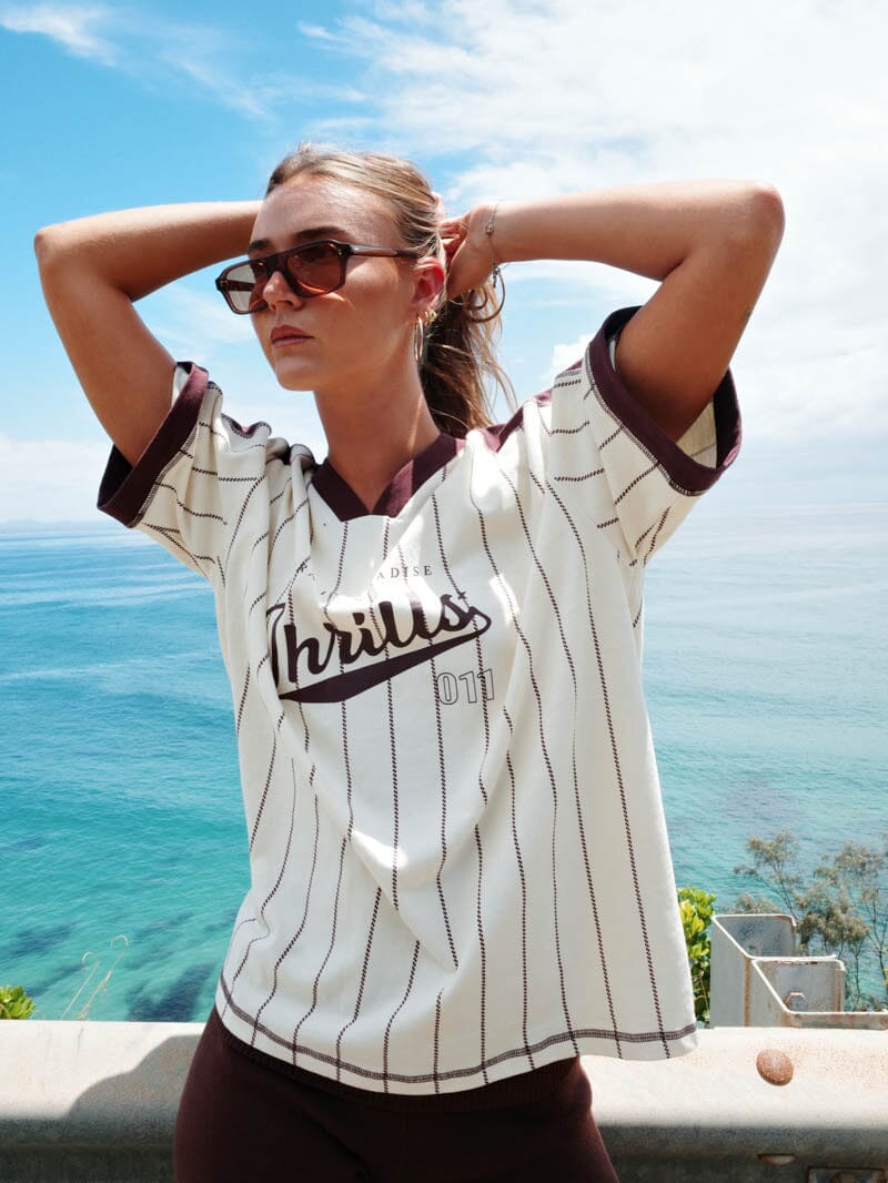Woman wearing a striped jersey with 'Thrills' text by the ocean