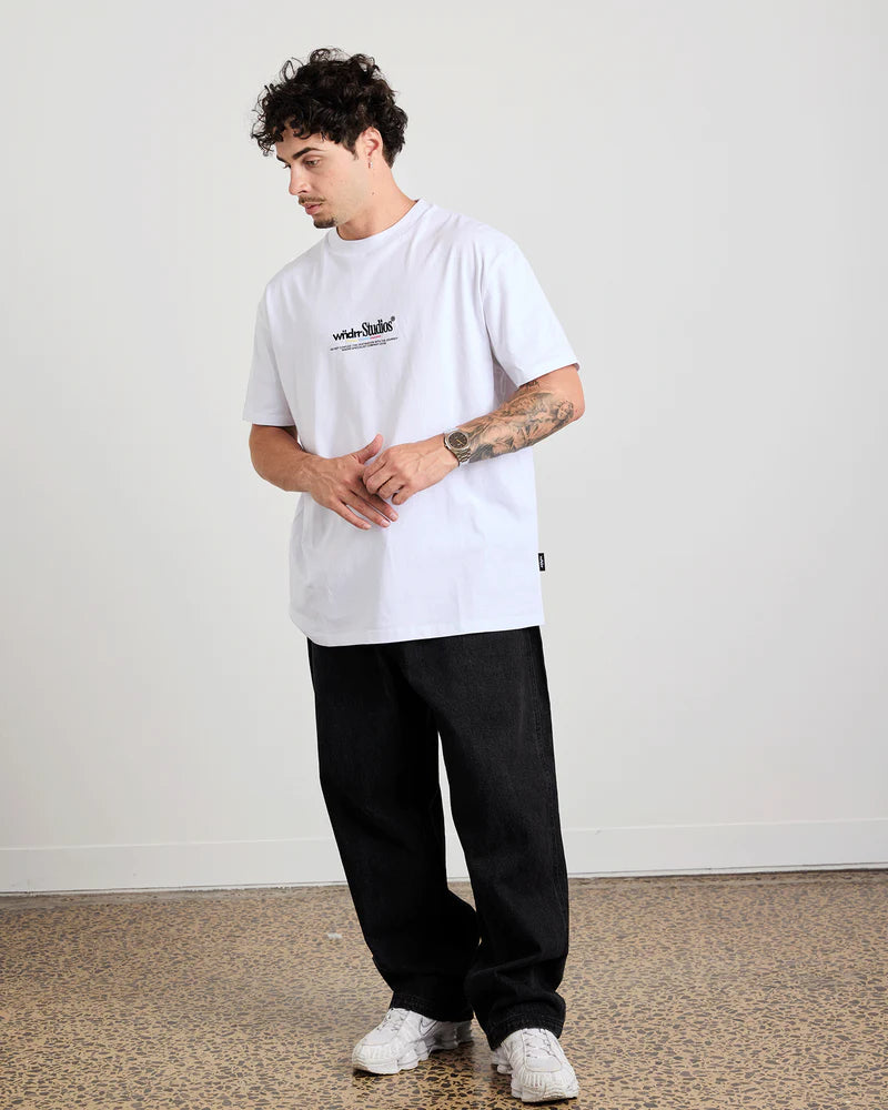 Person wearing a white wndrr t-shirt and black pants standing against a plain background