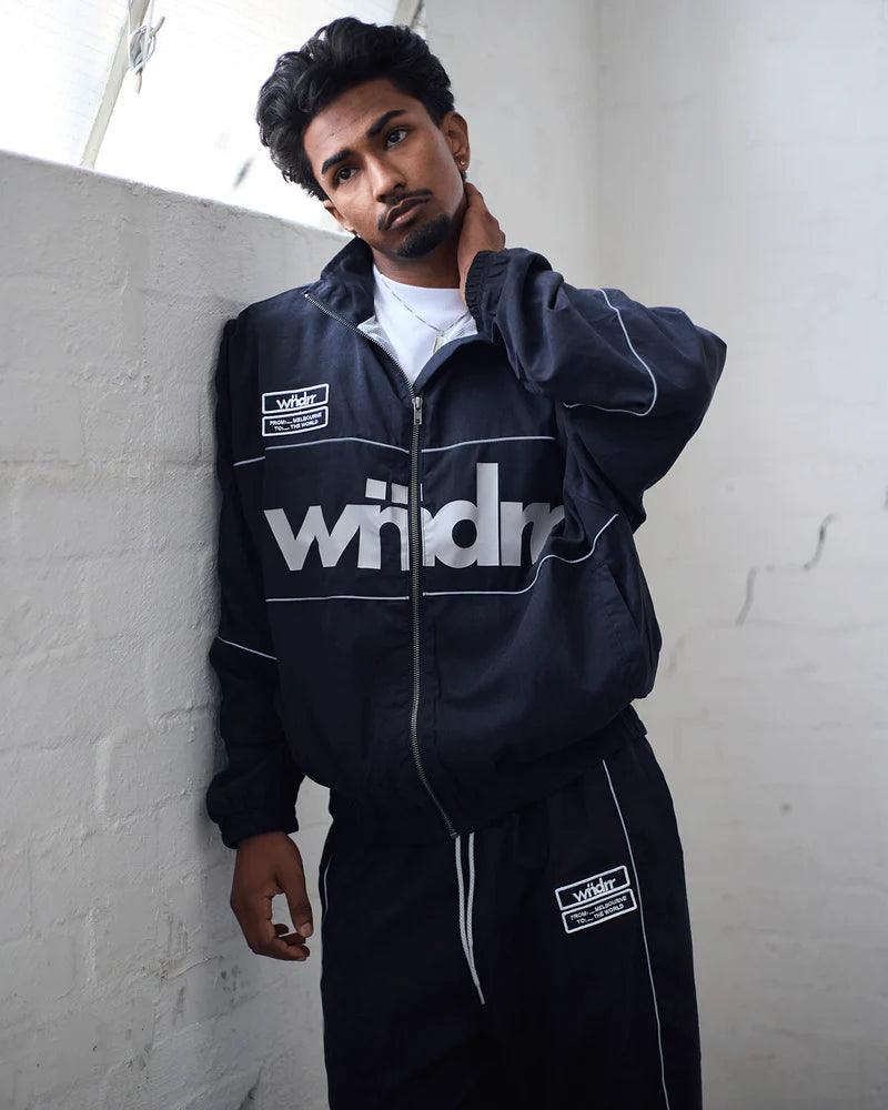 Person wearing a black tracksuit with 'wndrr' branding against a white wall.